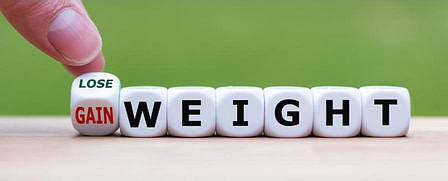 lose or gain weight Small blocks spell out the word "weight" while fingers hold another small block on it's edge exactly between to sides with one saying Lose and the other Gain in front of the word weight.