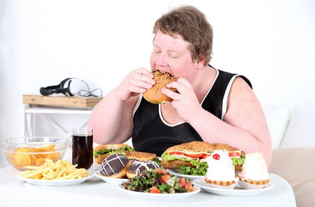 standard american diet An overweight person eating a variety of processed foods.
