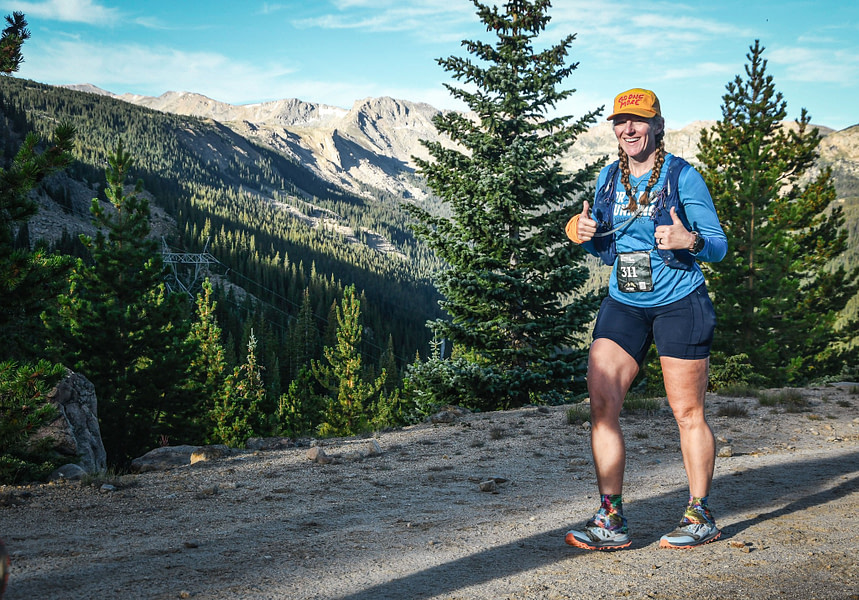 Heather at Leadville Heather Daunis giving thumbs up with mountains in the background and wearing a PRMD Running shirt while running Leadville 100.